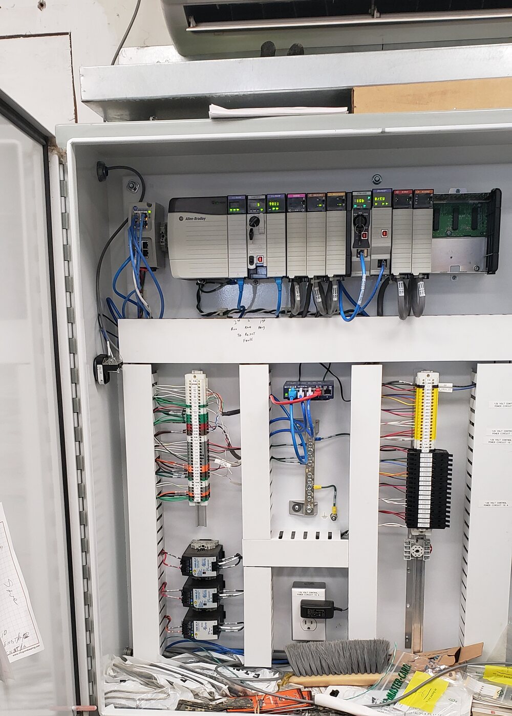 An open control cabinet containing an Allen-Bradley controller, I/O modules, network connections, and field wiring.